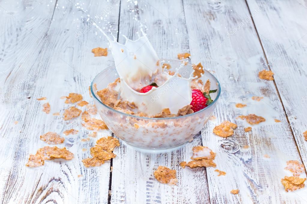 Strawberry falling in a bowl with milk and cereals.