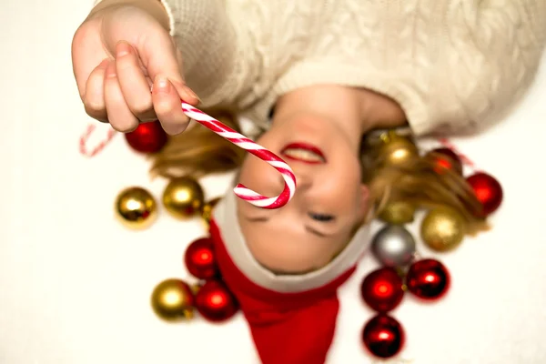 Schöne Blondine mit einem Weihnachtsbonbon auf einem weißen Rücken liegend — Stockfoto