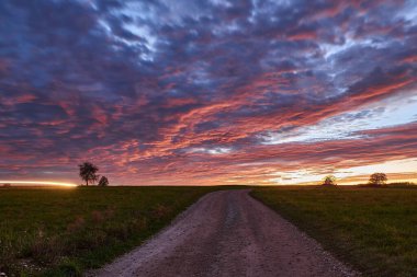 Issız bir arazide dramatik bir gün batımının uzun görüntüsü. Yeşil bir çayırda kırmızı bulutlarla gün batımı.