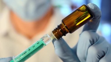 Yüz maskeli bir araştırmacı şırıngayı ilaçla dolduruyor. Şırıngayı aşıyla dolduran yüz maskeli bir sağlık görevlisine yakın çekim. Doktor elinde bir ilaç şişesi ve aşılı bir şırınga tutuyor..