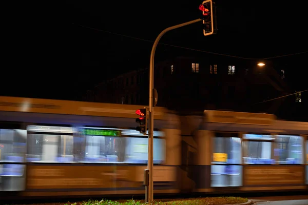 Moving tramway by night. Moving streetcar at night. Blurry tramway at night passes by a red street light.