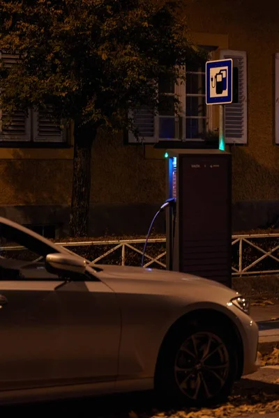 Electric car plugged into a charging station at night. Electric car plugged into a charging station for electric vehicles at night. Charging an electric car over night.