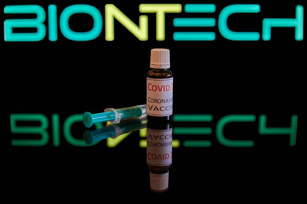 Munich/Bavaria/Germany - 11/16/2020: Coronavirus vaccine and a syringe on a black glossy surface.