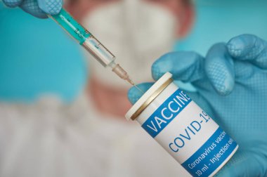 Yüz maskeli araştırmacı şırıngayı aşıyla dolduruyor. Bir şırıngayı koronavirüs aşısıyla dolduran yüz maskeli bir araştırmacının yakın çekimi..