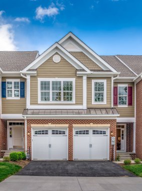 Aerial view of a double gable roof with triangle gable decoration and elegant colonial white round gable vent on a beige shake and shingle siding roof on a luxury town home with blue cloudy sky clipart