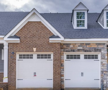 İki tek araba, çatısı yatakhane pencereli ve gri fırtınalı gökyüzü olan yeni bir Amerikan konağının kapılarını kapatıyor.