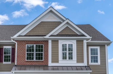 Ters çift gable, lüks, tek kişilik aile evine yakın çekim. Kare tek cam gable penceresi. Geleneksel evin çatı çizgisi, bir gable bir yönde çalışan ters gable diğer yönde çalışan.