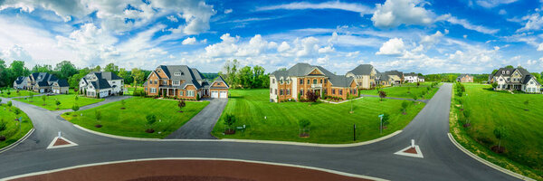 Aerial panorama of new neighborhood street with luxury real estate properties, mansions, brick covered villas with a roundabout and blue sky in Maryland USA