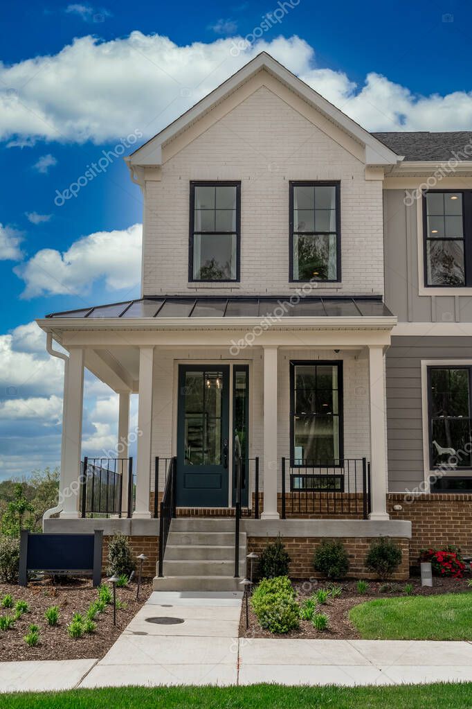 Corner unit with white siding wrap around covered porch on a new development street with blue cloudy sky