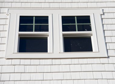 Double hung window with fixed top sash and bottom sash that slides up, sash divided by white grilles a surrounded by white elegant frame  horizontal white shingle siding on new construction residence clipart