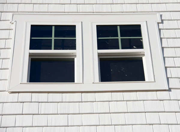 Double hung window with fixed top sash and bottom sash that slides up, sash divided by white grilles a surrounded by white elegant frame  horizontal white shingle siding on new construction residence