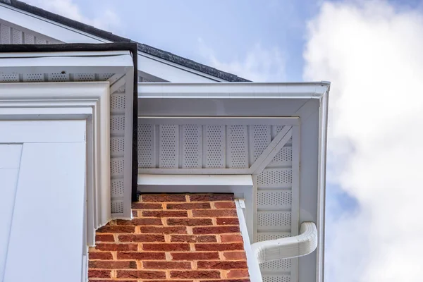 Close up of white frame gutter guard system, eaves through, fascia, drip edge, colonial white soffit with ventilation, brick facade siding on a luxury American single family home neighborhood USA