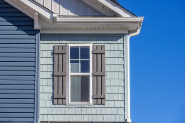 Close up view of classic double hung sash window with wooden shutters on a newly build house with green shake and shingle siding , white gutter system in America blue sky clipart