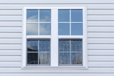 Stand alone double hung window with fixed top sash and bottom sash that slides up, sash divided by three white grilles, surrounded by lintel and frame, decorative trim on a new residence clipart
