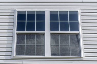 Double hung window with fixed top sash and bottom sash that slides up, sash divided by two white grilles, surrounded by white elegant frame  horizontal white vinyl siding on new residence clipart