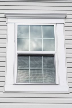 Double hung window with fixed top sash and bottom sash that slides up, sash divided by two white grilles, surrounded by white elegant frame  horizontal white vinyl siding on new residence clipart