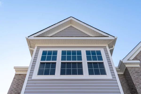 Çift askılı pencere, yukarı doğru kayan sabitlenmiş üst kuşak ve alt kuşak, beyaz ızgaralar tarafından bölünmüş beyaz zarif bir çerçeve yatay vinil kaplama, bir gable ve soffit altında
