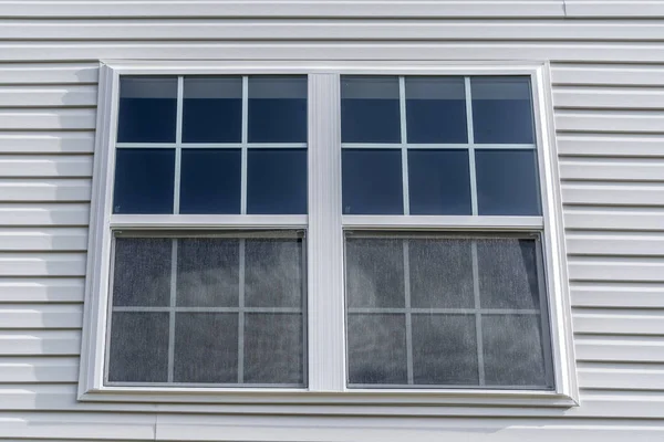 Double hung window with fixed top sash and bottom sash that slides up, sash divided by two white grilles, surrounded by white elegant frame  horizontal white vinyl siding on new residence