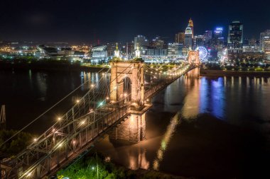 Cincinnati 'nin panoramik gece manzarası Ohio nehri üzerindeki tarihi Roebling asma köprüsü