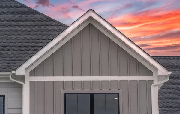 White frame gutter guard system, with dark gray horizontal vinyl siding, white accents, fascia, soffit, on a pitched roof attic at a luxury American single family home dramatic colorful sunset sky