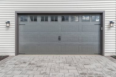 Gray two single car garage door framed with architectural stone to add accent, with transom light windows divided by muntins grills  clipart