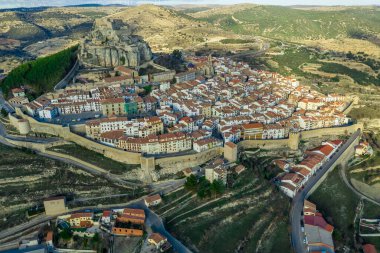 Morella 'nın hava günbatımı manzarası, ortaçağ duvarlı kasabası yarı daire şeklinde kuleler ve İspanya' da kayalıklarda bir kale tarafından kargalanan kapı evleri.