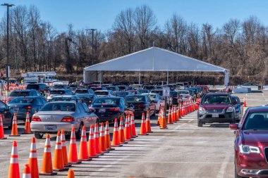 Maryland 'deki toplu aşılama alanında turuncu koniler tarafından ayrılmış kayıt çadırına varmadan önce sırada bekleyen arabalar var.