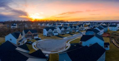 Curving suburban neighborhood dead end street with newly constructed single family homes in an American  residential real estate development with stunning orange, pink, red, blue, yellow sunset clipart