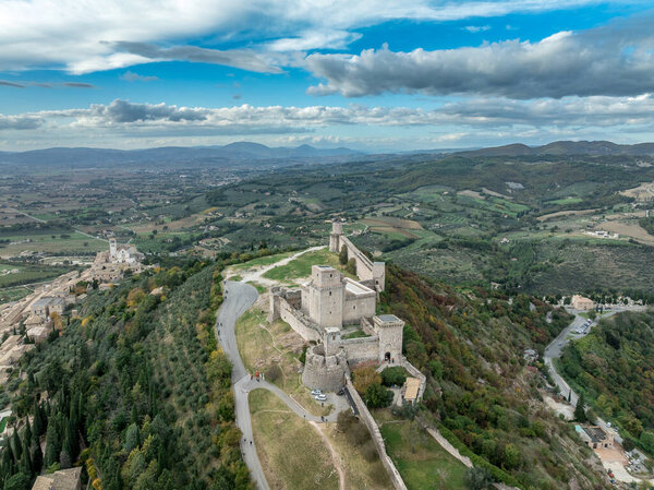 An aerial view of Assisis Rocca Maggiore fortress crowning the hill above terracotta roofs and Umbria