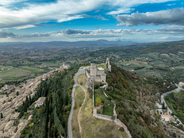 An aerial view of Assisis Rocca Maggiore fortress crowning the hill above terracotta roofs and Umbria