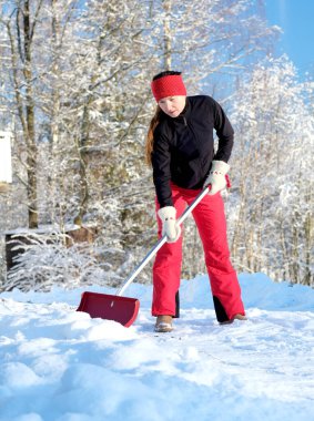 Kırmızı pantolonlu, mavi gökyüzüne kar kürekleyen mutlu genç kadın.