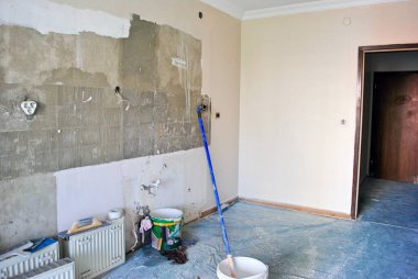 Kovalar ve fırçalarla kısmen boyanmış mutfak tadilatı sürüyor. Krem rengi beton duvar.