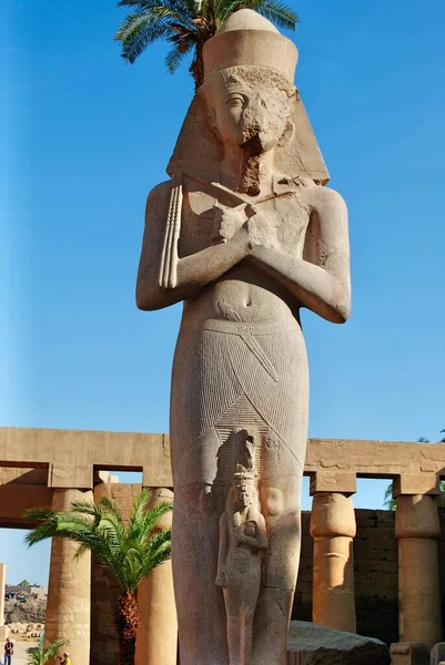 Unidentified male tourist walking towards the Colossal statue of pharaoh Rameses II and Princess-Queen Meritamen at Luxor Temple, dated back 1400 BC. Luxor Egypt. UNESCO World Heritage Site. Royalty Free Stock Photos