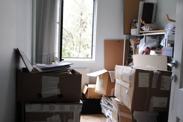 Concetto di imballaggio in movimento. Una stanza piena di scatole di cartone disordinate con una finestra aperta. Fotografia Stock