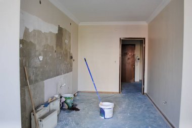 Mutfak duvarında kapı, kiremit ve musluk olmadan tadilat yapılıyor. Küçük aletlerle kirli radyatörler bırakmış. Ev tadilatı. Ev onarımı.