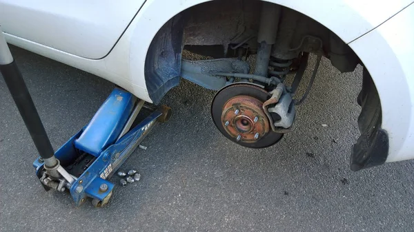 Car raised on jack. Changing flat tire on your own. Wheel replacement. Outdoor auto repair shop. Service center. Wheel alignment. Tyre balance. Vehicle disc brake. Repair automobile suspension.