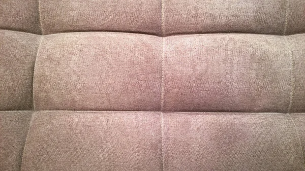 Detail of upholstery of modern chair, armchair, sofa, pouf or pillow. Brown color. Premium luxury fabric. Home decor. Design interior. Natural beige hue backdrop. Close-up. Furniture Manufacturing.