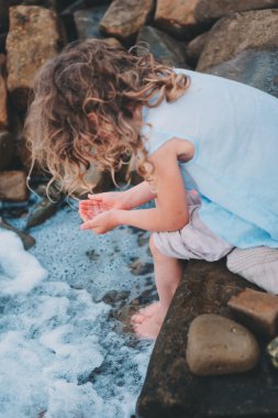 mutlu bir çocukluk kız su ile taş sahilde oynarken. Çocuklar seyahat deniz, rahat tatilde.