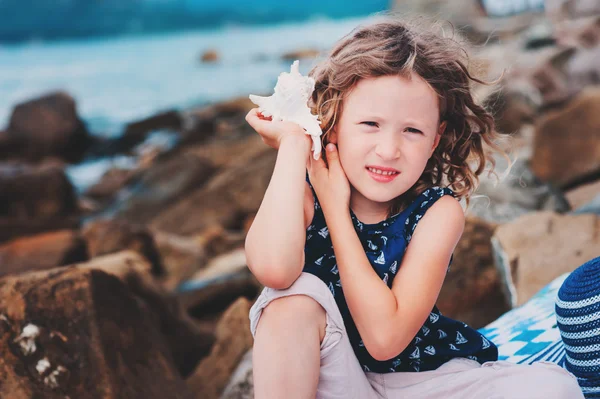 Çizgili şapkalı mutlu çocuk kız sahilde oynarken ve deniz kabuğu dinlemek. Yaz tatilinde seyahat. — Stok fotoğraf