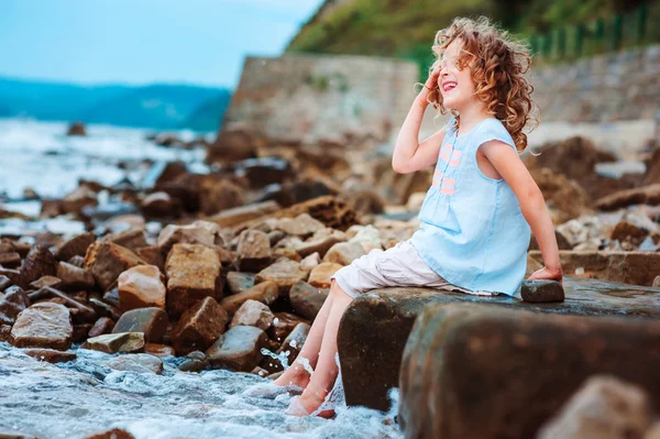 Niña feliz jugando con agua en la playa de piedra. Acogedoras vacaciones en el mar, viajando con niños . — Foto de Stock