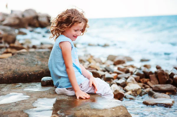 Niña feliz jugando con agua en la playa de piedra. Acogedoras vacaciones en el mar, viajando con niños . — Foto de Stock
