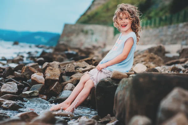 Niña feliz jugando con agua en la playa de piedra. Acogedoras vacaciones en el mar, viajando con niños . — Foto de Stock