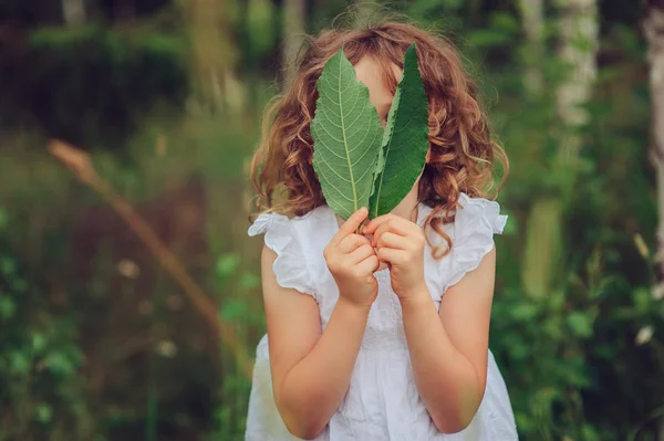 Niña jugando con hojas en el bosque de verano. Exploración de la naturaleza con niños. Actividades rurales al aire libre . — Foto de Stock