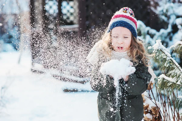 Happy child girl playing with snow on snowy winter walk on backyard, making snowballs in the garden — Stock Photo, Image