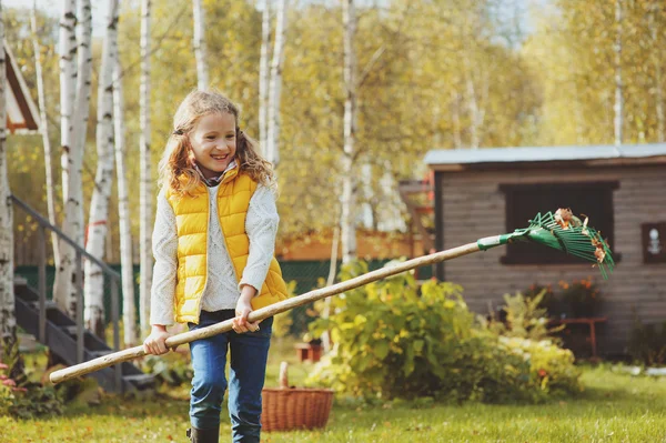 Bambina felice giocando piccolo giardiniere in autunno e raccogliendo foglie nel cestino. Lavori stagionali in giardino. Pulizia del cortile . — Foto Stock