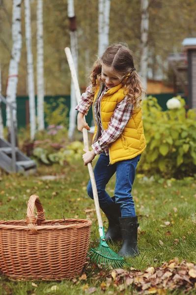 Happy child girl playing little gardener in autumn and picking leaves into basket. Seasonal garden work. Backyard cleaning. — Stock Photo, Image