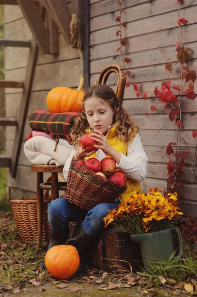 Glückliches Kind, das auf dem Bauernhof frische Äpfel pflückt. Landleben-Konzept, gemütliche saisonale Dekorationen auf Hintergrund — Stockfoto