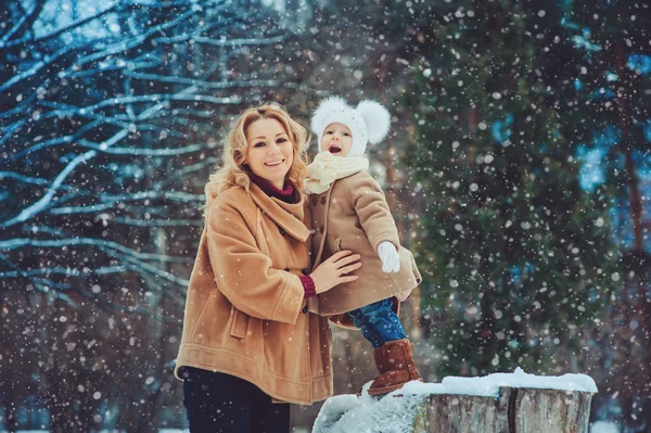 Happy mother and baby daughter walking in snowy winter park. Christmas family time. — Stock Photo, Image