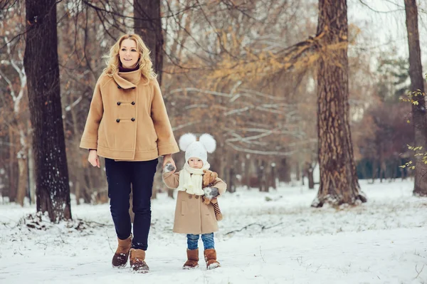 Happy mother and baby daughter walking in snowy winter park. Christmas family time. — Stock Photo, Image