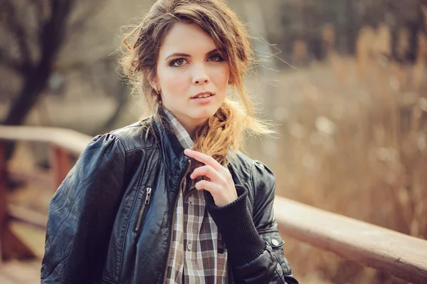 Autumn outdoor portrait of young beautiful woman with natural makeup in leather jacket and plaid shirt, soft vintage toned — Stock Photo, Image